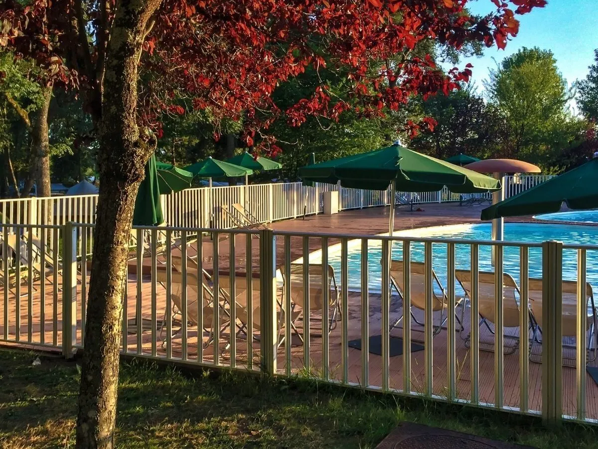 An aluminium pool safety fence around a pool deck with sun lounges and green umbrellas